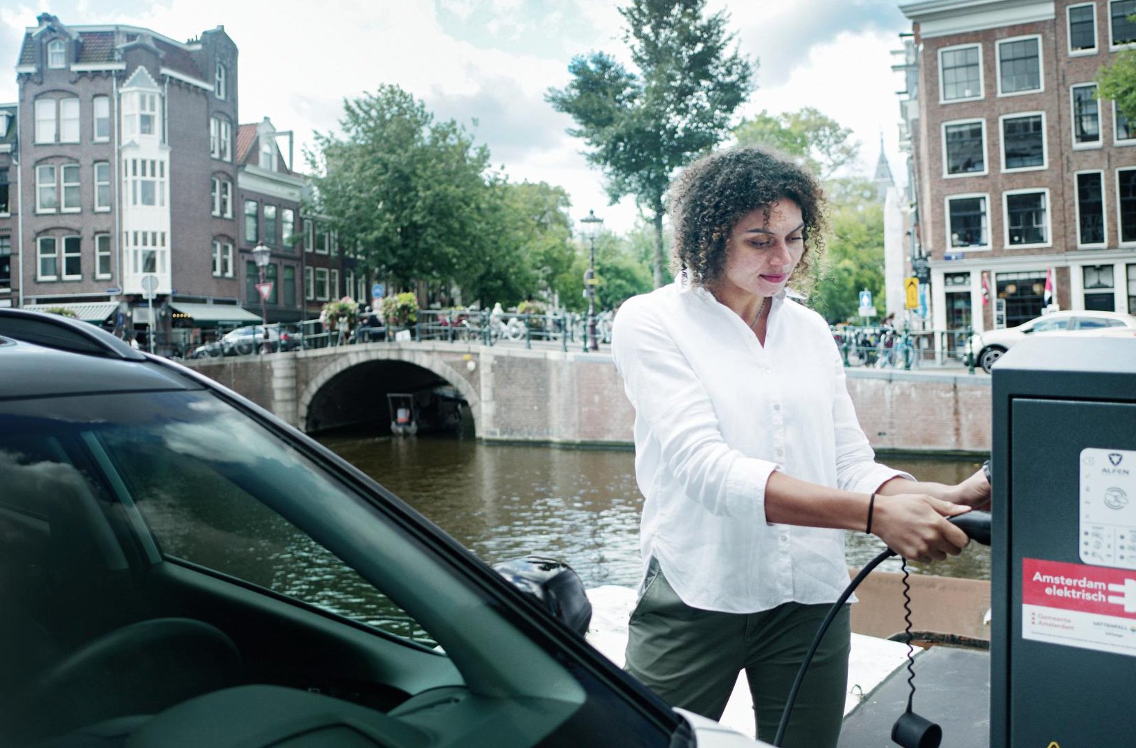Woman charging an electric car next to a canal in Amsterdam. Woman charging an electric car next to a canal in Amsterdam.