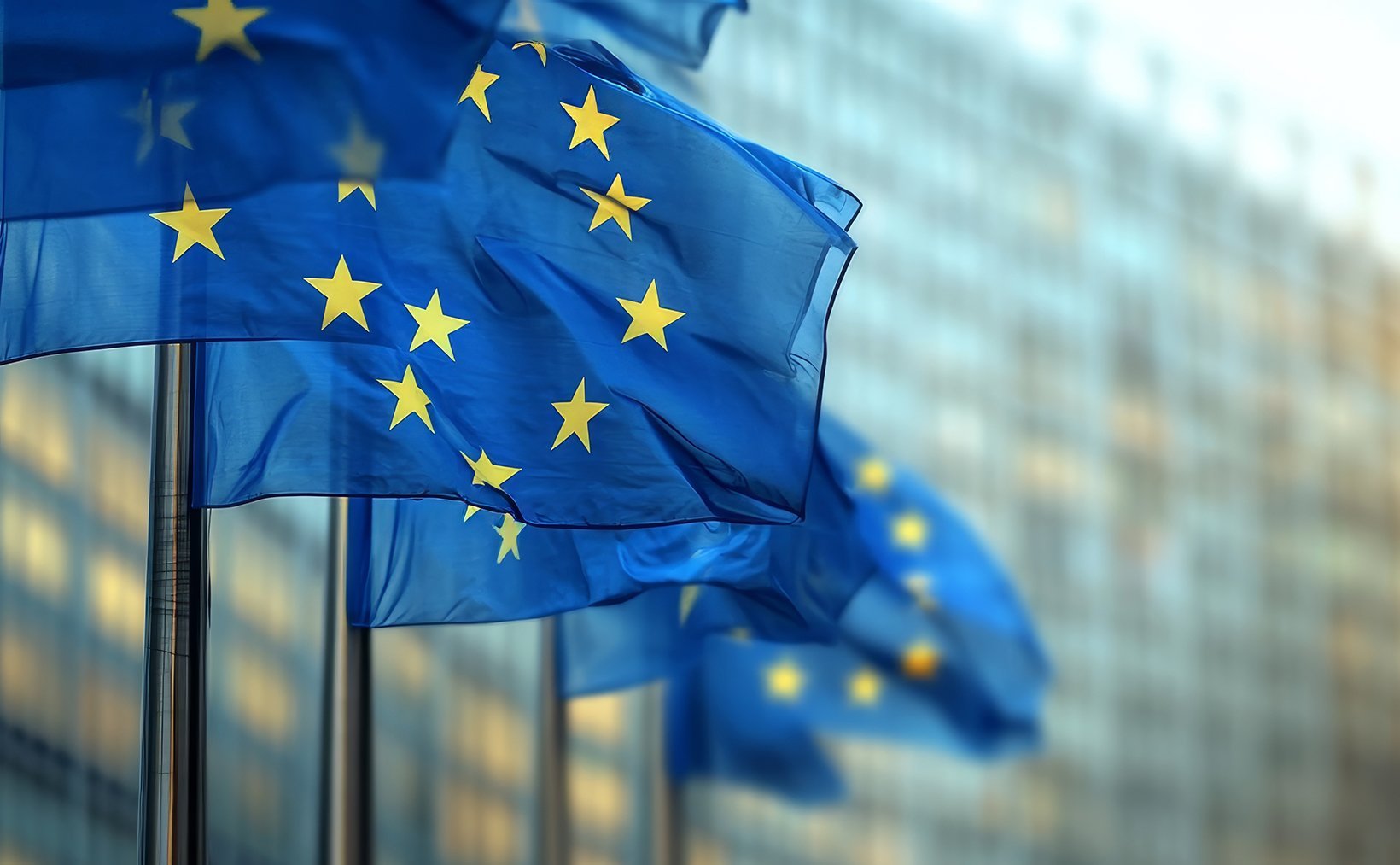 European Union flags flying outside a modern glass building. European Union flags flying outside a modern glass building.