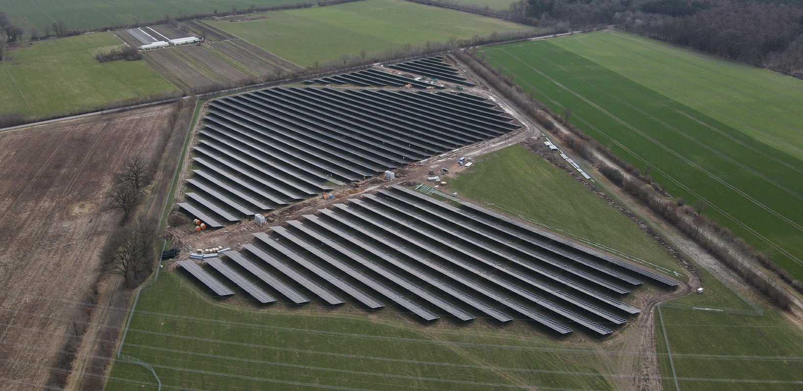 Aerial view of Juliusburg/Krukow solar farm with rows of dark panels set among green and brown agricultural fields.