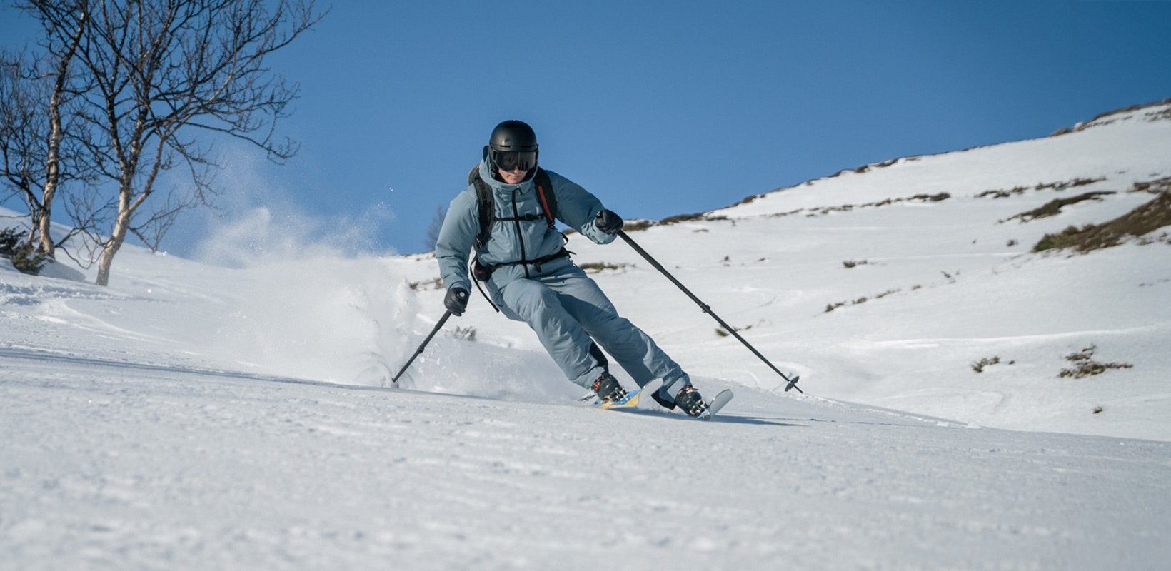 Skier carving downhill through fresh snow on a sunny, open mountain slope.