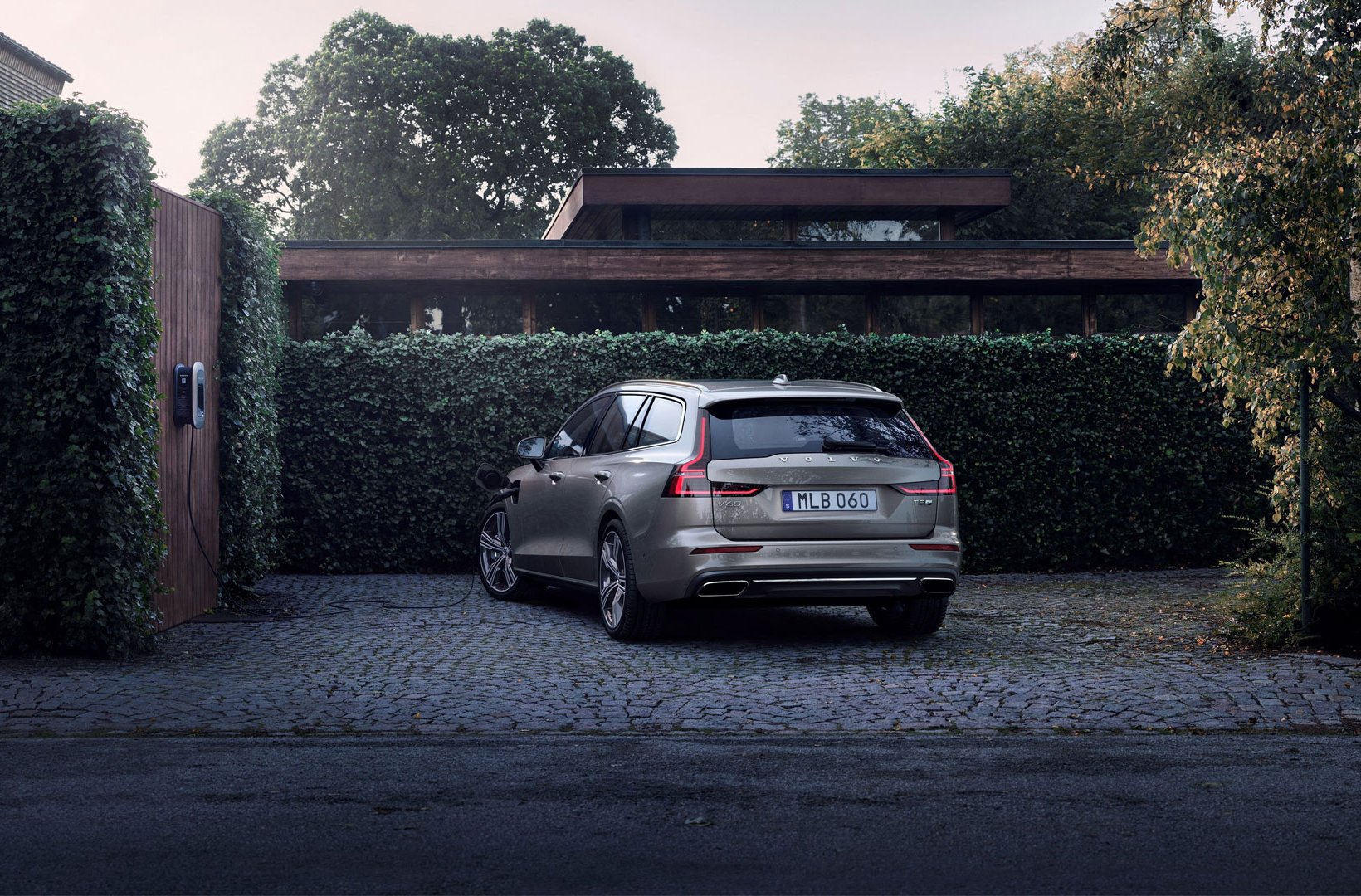 A plug-in hybrid Volvo being charged in front of a house 