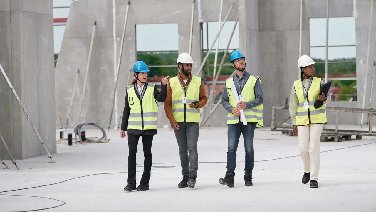 Four people wearing helmets and high-visibility vests on a building site.