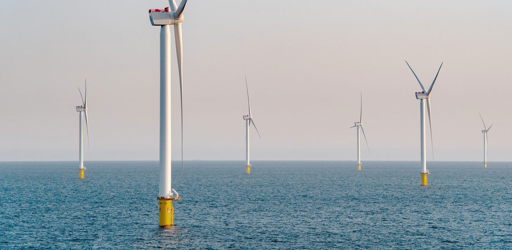 Six offshore wind turbines in a calm blue sea.