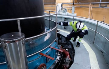 An employee in protective clothing kneeling down to check a piece of equipment in Harsprånget hydro power plant.