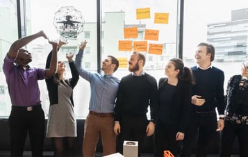 A group of people in an office reaching for a flying drone.