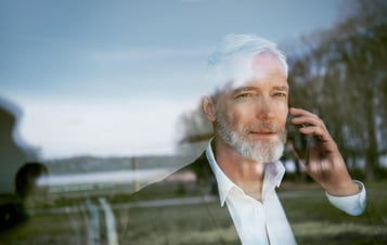 A man making a phone call, seen through glass with reflections of water and trees. A man making a phone call, seen through glass with reflections of water and trees.