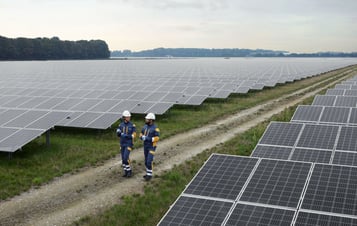 Two employees in protective clothing walking in a solar farm.