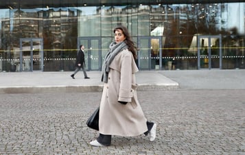 Woman in a long coat walking across a paved area in front of a modern glass building. Woman in a long coat walking across a paved area in front of a modern glass building.