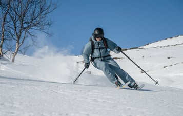 Skier carving downhill through fresh snow on a sunny, open mountain slope.