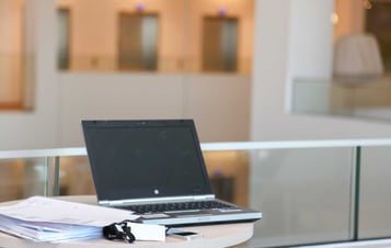 A laptop computer next to a pile of papers in a modern office environment.