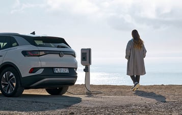 A woman standing by the sea while charging her electric car