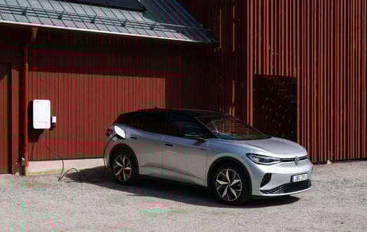 A Volkswagen connected to a bidirectional charger outside a red building. A Volkswagen connected to a bidirectional charger outside a red building.