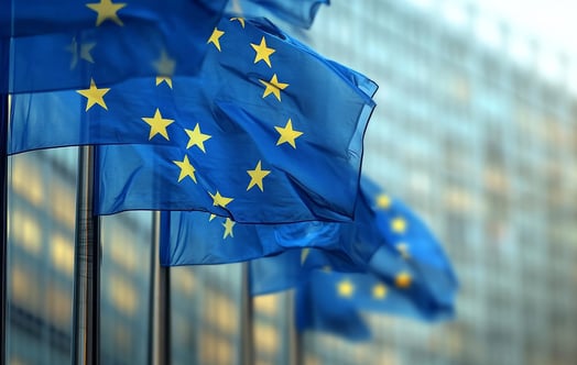 European Union flags flying outside a modern glass building.