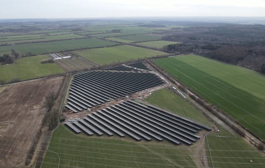 Aerial view of Juliusburg/Krukow solar farm with rows of dark panels set among green and brown agricultural fields.