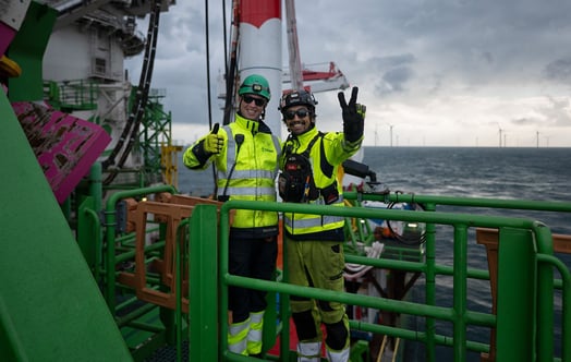 Two workers in high-visibility protective clothing standing on an offshore platform.