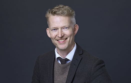 Studio portrait of Ronny Brunstad, Managing Director Vattenfall Norway, in a dark blazer, sweater and tie against a plain dark background.