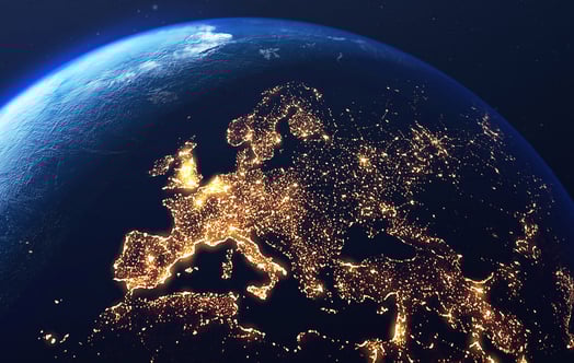 A view of Earth from space showing Europe at night, illuminated by thousands of city lights, with the curve of the planet visible against the dark sky.