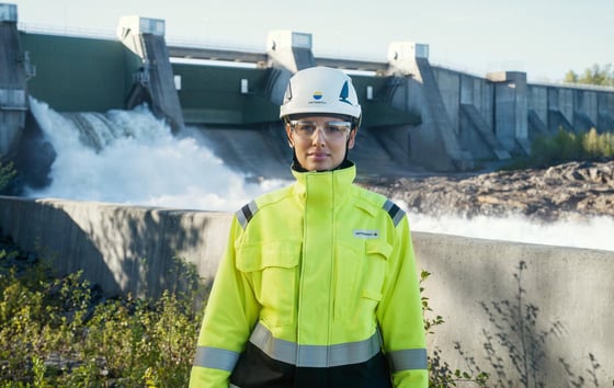 Woman in high-visibility safety clothing and helmet standing in front of a hydro power plant. Woman in high-visibility safety clothing and helmet standing in front of a hydro power plant.