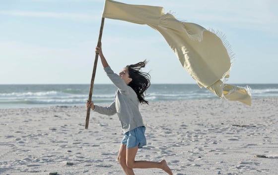 Girl running on a beach with a makeshift flag