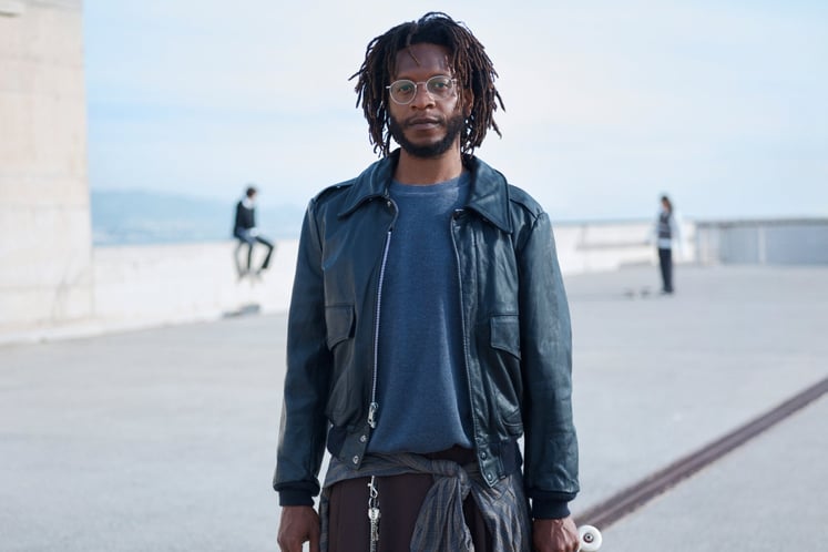 Man with dreadlocks holding a skateboard, looking into the camera, with concrete blocks in a skatepark behind him. Man with dreadlocks holding a skateboard, looking into the camera, with concrete blocks in a skatepark behind him.