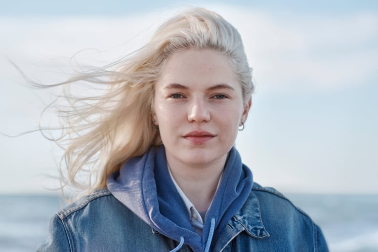 Woman with blond hair blowing in the wind, looking into the camera, with the sea behind her. Woman with blond hair blowing in the wind, looking into the camera, with the sea behind her.