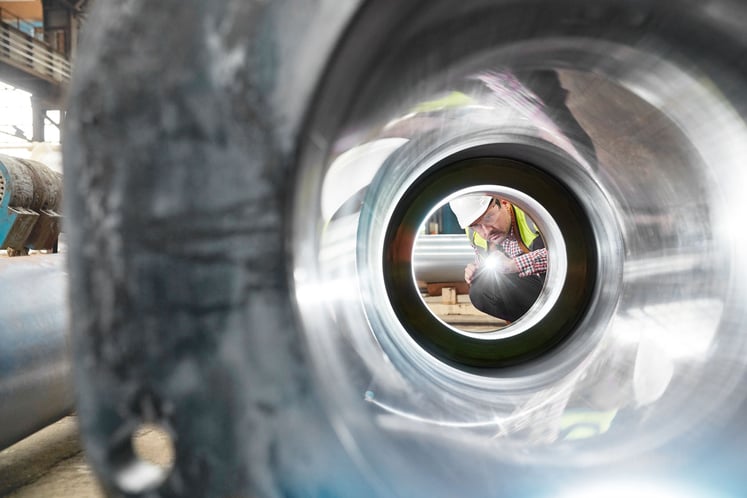 A man holding a torch and peering into a metal pipe A man holding a torch and peering into a metal pipe