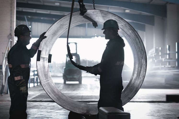 Two men stand in front of a pipe which is lifted into the air