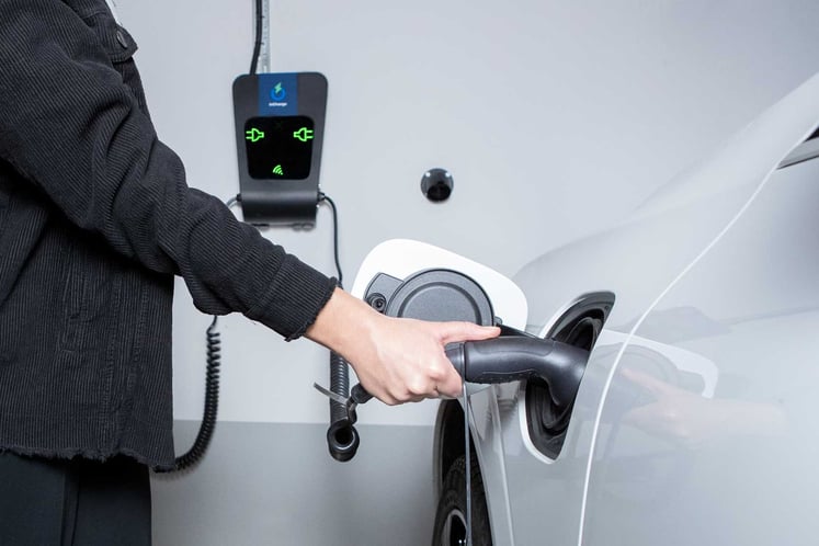 Woman plugs charging cable into electric vehicle
