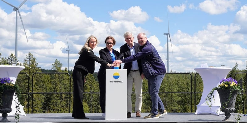 Representatives from Vattenfall, Eksjö Municipality and Volvo press a button on a podium bearing the Vattenfall logo, on an outdoor stage with wind turbines and a forest in the background.