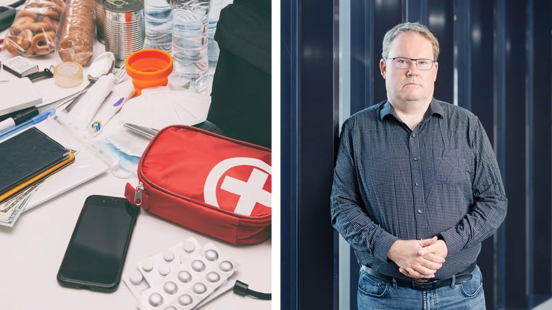 A split image. On the left, various emergency-preparedness items are spread out on a table, including a red first‑aid kit with a white cross, blister packs of pills, a smartphone, passports with cash, water bottles, and assorted small tools and supplies. On the right, Malkus Lindroos stands indoors in front of dark vertical panels, wearing a long‑sleeve patterned shirt and jeans with their hands loosely clasped in front of them.