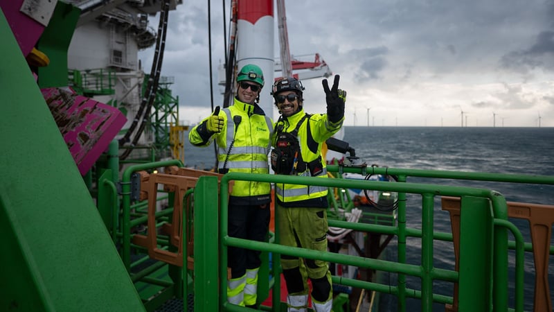 Two workers in high-visibility protective clothing standing on an offshore platform.
