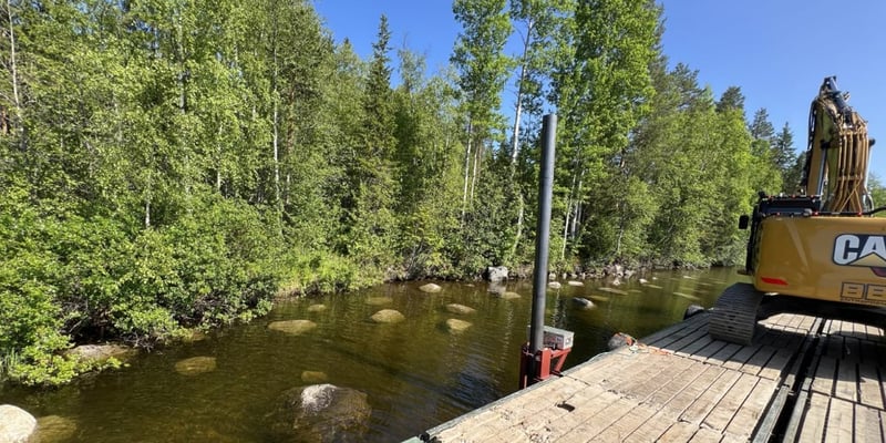 Work barge with an excavator at a stone-lined riverbank.