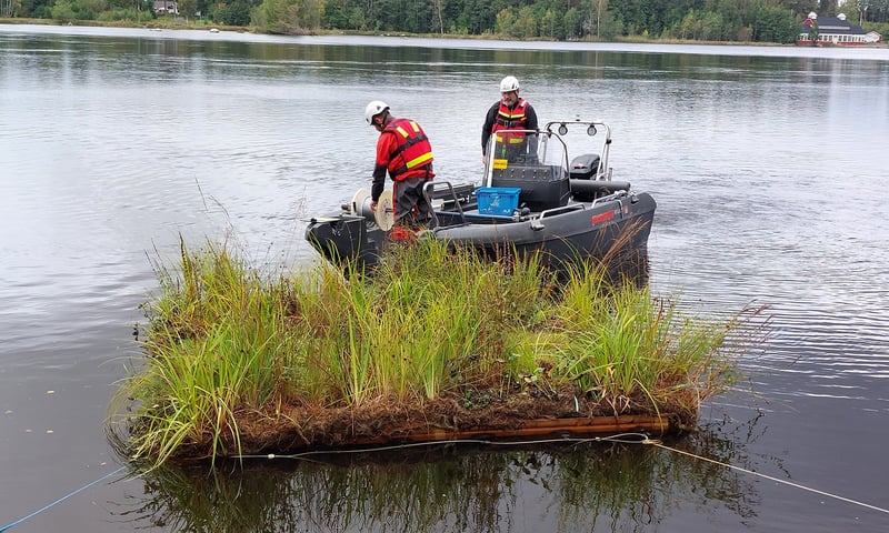 Floating island with vegetation in a river, positioned in front of a small work boat. Photo: Maidul Choudhury.