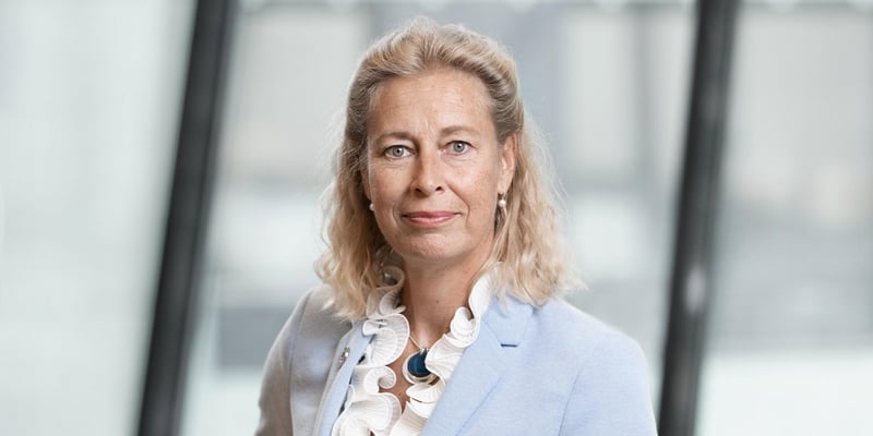 Annika Ramsköld, Vattenfall's Head of Sustainability, wearing a light blue blazer and white ruffled blouse, standing indoors with large windows in the background.