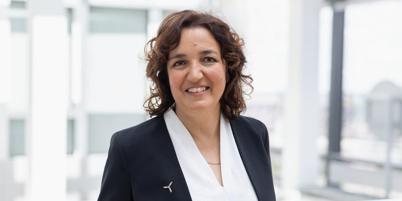 Catrin Jung, Head of Business Area Wind, wearing a dark blazer with a small lapel pin and a white blouse, standing in a bright, modern office environment.