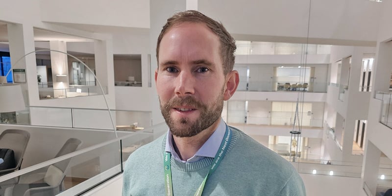 Dag Wästlund, Section Manager, Data Science & AI, wearing a green sweater and lanyard standing in a bright, modern office atrium with glass railings and open floors.
