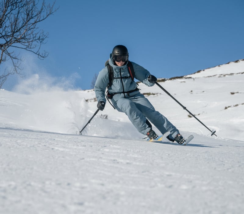 Skier carving downhill through fresh snow on a sunny, open mountain slope.