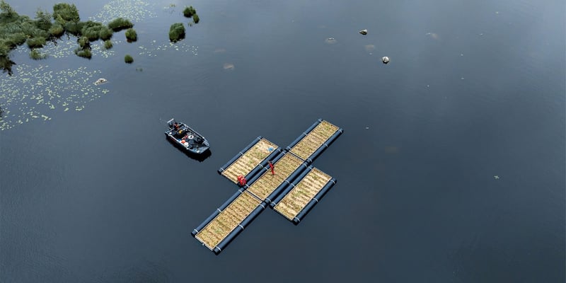 Aerial view of a floating wetland platform on calm water, with a small workboat alongside.