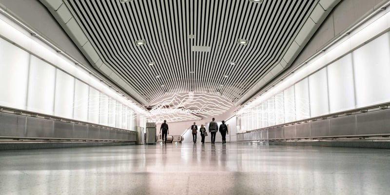 People walking through a wide indoor corridor with illuminated wall panels and ceiling lights. People walking through a wide indoor corridor with illuminated wall panels and ceiling lights.