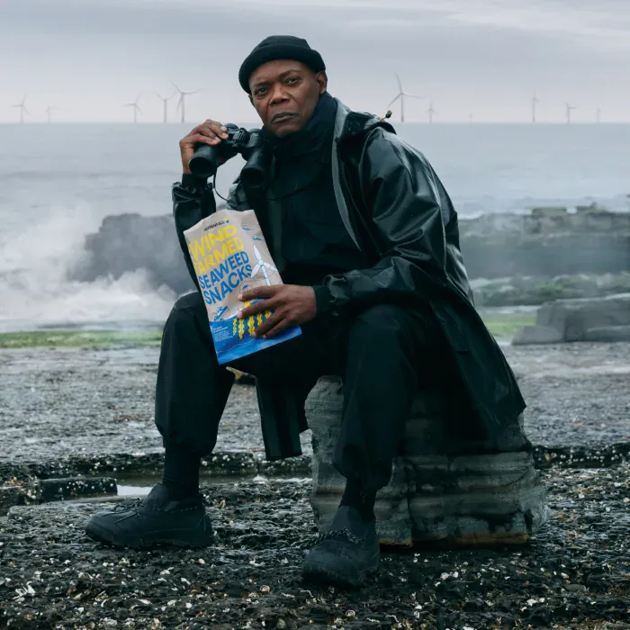 Samuel L. Jackson zit op een rots met in de ene hand Wind Farmed Seaweed Snacks en in de andere een verrekijker. Op de achtergrond de wilde zee en enkele windturbines.
