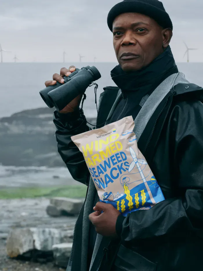 Samuel L. Jackson staht auf den Klippen und  hält eine Tüte der "Wind Farmed Seaweed Snacks" in der einen und einem Fernglas in der anderen Hand. Im Hintergrund befinden sich das wilde Meer und mehrere Windturbinen.