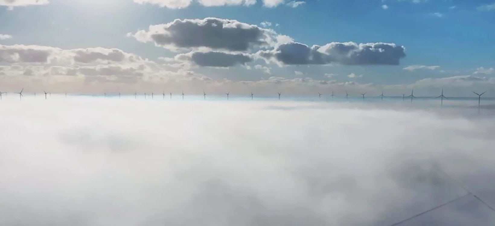 Eine Reihe von Windkraftanlagen, die über die Wolken hinausragen.