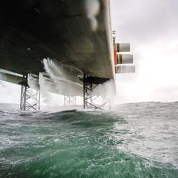 Wellen schlagen gegen das Fundament einer Anlage im Offshore-Windpark Sandbank.
