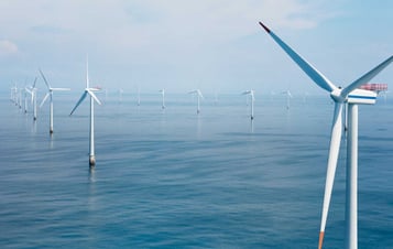 Offshore-Windpark mit mehreren Windkraftanlagen, die sich über ruhiges Meer unter leicht bewölktem Himmel erstrecken.