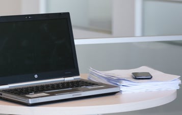 Ein Laptop und ein Stapel Papiere auf einem Schreibtisch in einem Büro.