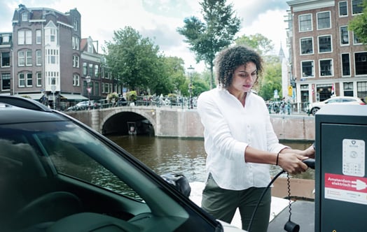 Eine Frau lädt ein Elektroauto neben einem Kanal in Amsterdam auf. Eine Frau lädt ein Elektroauto neben einem Kanal in Amsterdam auf.