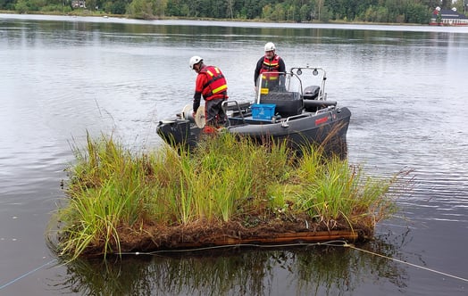 Schwimmende Insel mit Vegetation in einem Fluss, platziert vor einem kleinen Arbeitsboot. Foto: Maidul Choudhury.
