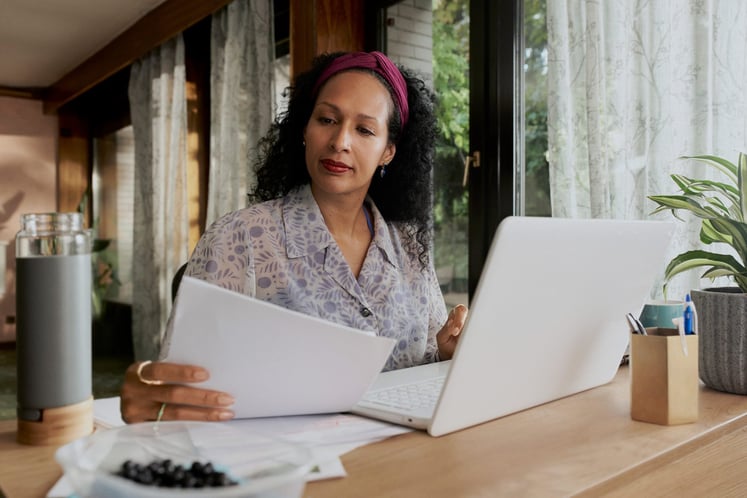 Eine Frau an einem Tisch mit einem Stapel Papiere und einem Laptop
