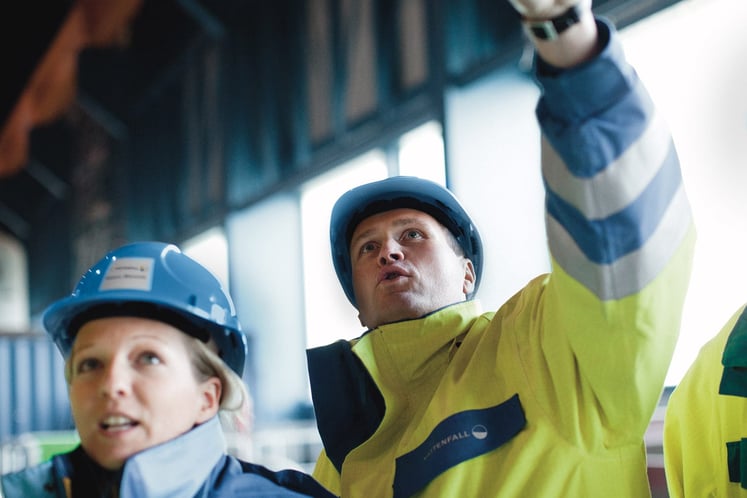Arbeitende mit Helmen und Warnkleidung blicken nach oben; eine Person zeigt in einem Gebäude. Arbeitende mit Helmen und Warnkleidung blicken nach oben; eine Person zeigt in einem Gebäude.