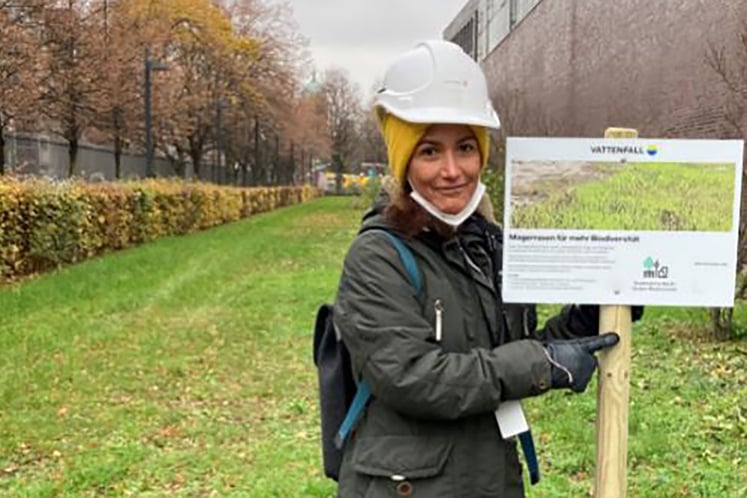 Gissela Riccio mit dem Hinweisschild "Magerrasen für mehr Biodiversität" am Vattenfall Wärme Standort Heizkraftwerk Mitte in Berlin 